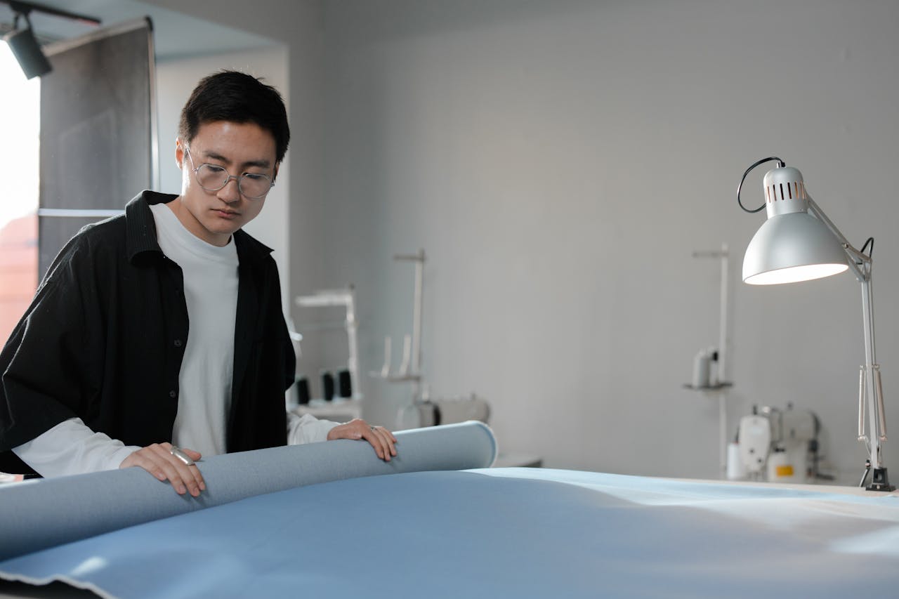 Fashion designer examining a blue fabric roll in a well-lit workspace.